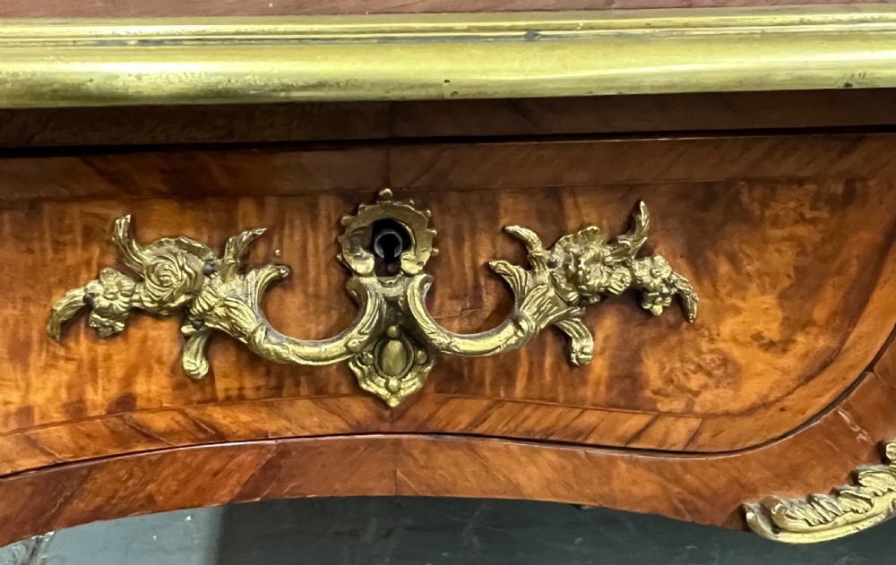 A nineteenth-century French bureau plat desk featuring wood marquetry, curved cabriole legs, ornate gilt-bronze mounts, three frieze drawers, and a leather inset writing top. View XVI