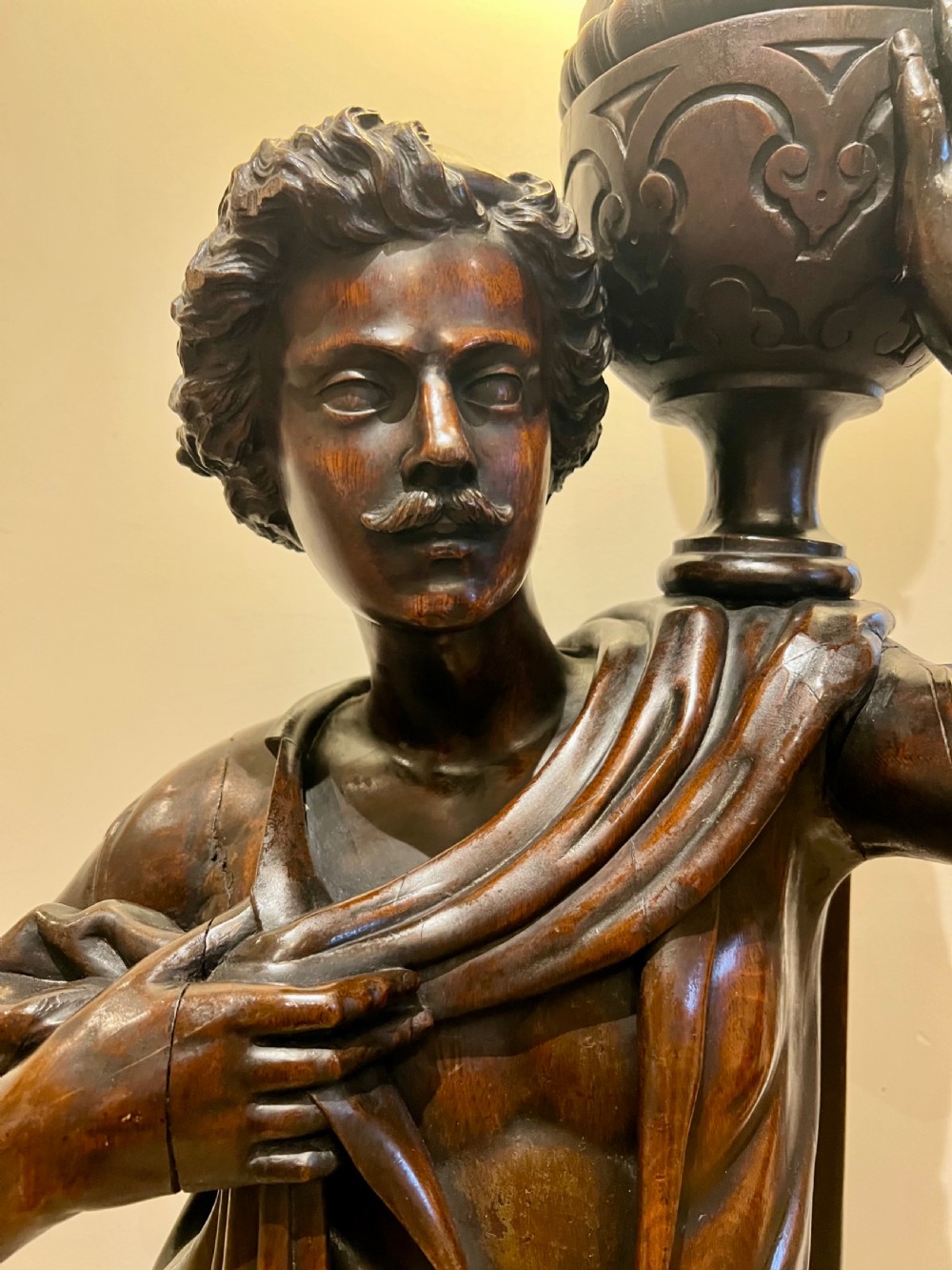 A 19th-century carved dark wood figural floor lamp depicting a draped male figure holding an illuminated flame glass urn on a octagonal base. View IV
