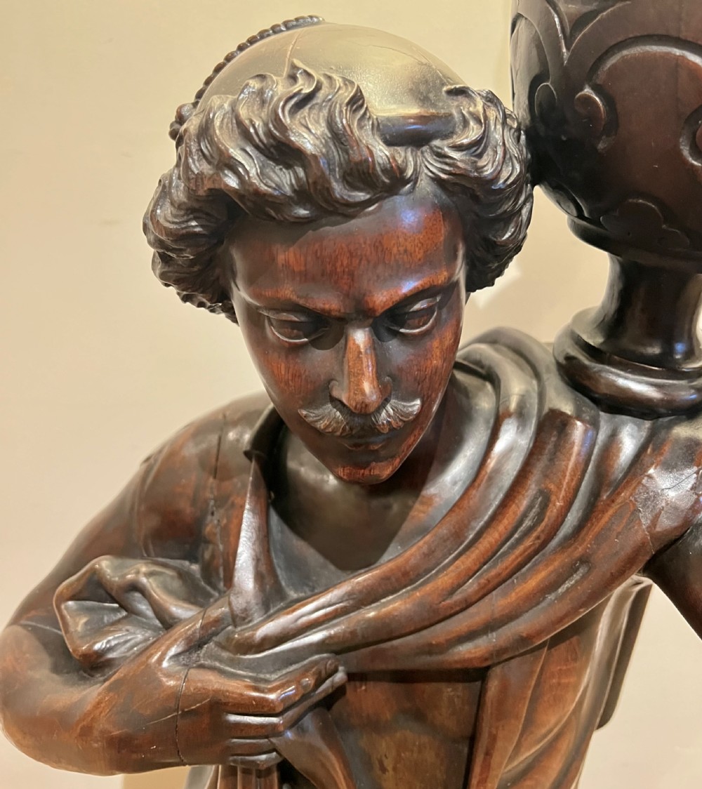 A 19th-century carved dark wood figural floor lamp depicting a draped male figure holding an illuminated flame glass urn on a octagonal base. View XII