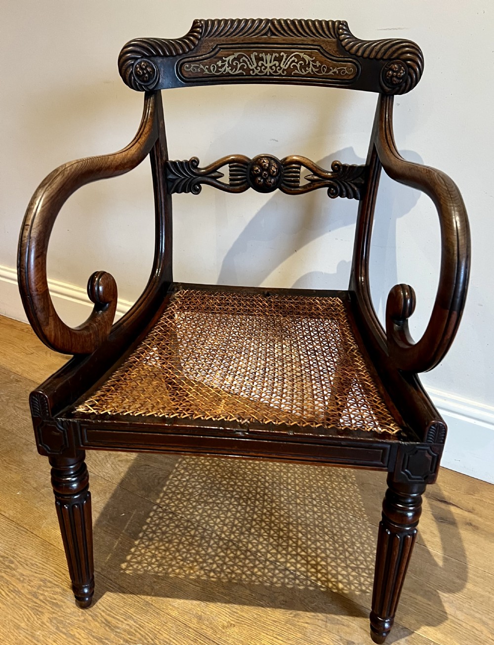 A Regency rosewood elbow chair featuring brass inlay along the top rail, curved scroll arms, a carved central splat, reeded front legs, and a colourful botanical upholstered seat. View II