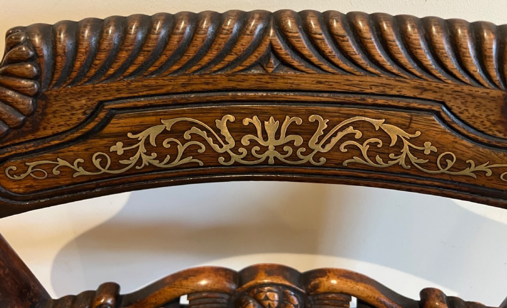 A Regency rosewood elbow chair featuring brass inlay along the top rail, curved scroll arms, a carved central splat, reeded front legs, and a colourful botanical upholstered seat. View X