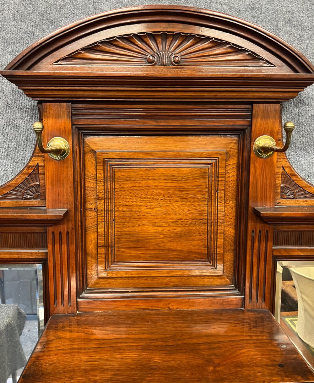 A tall Victorian carved walnut hall stand featuring brass coat hooks, bevelled mirrors, a central carved cupboard, and lower umbrella rails. View X