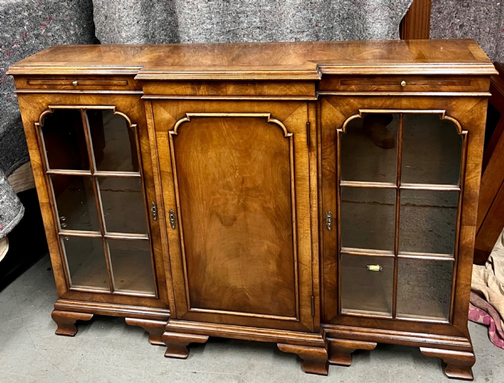 A low Queen Anne style walnut dwarf bookcase featuring a breakfront design with glazed side doors, a central veneered cupboard door, and bracket feet.