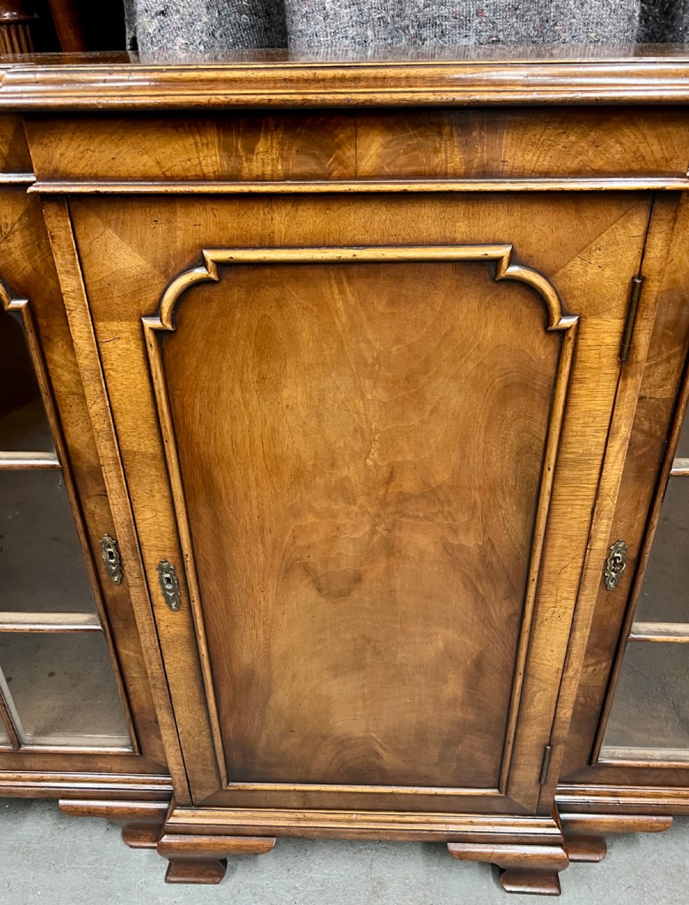 A low Queen Anne style walnut dwarf bookcase featuring a breakfront design with glazed side doors, a central veneered cupboard door, and bracket feet. View VI