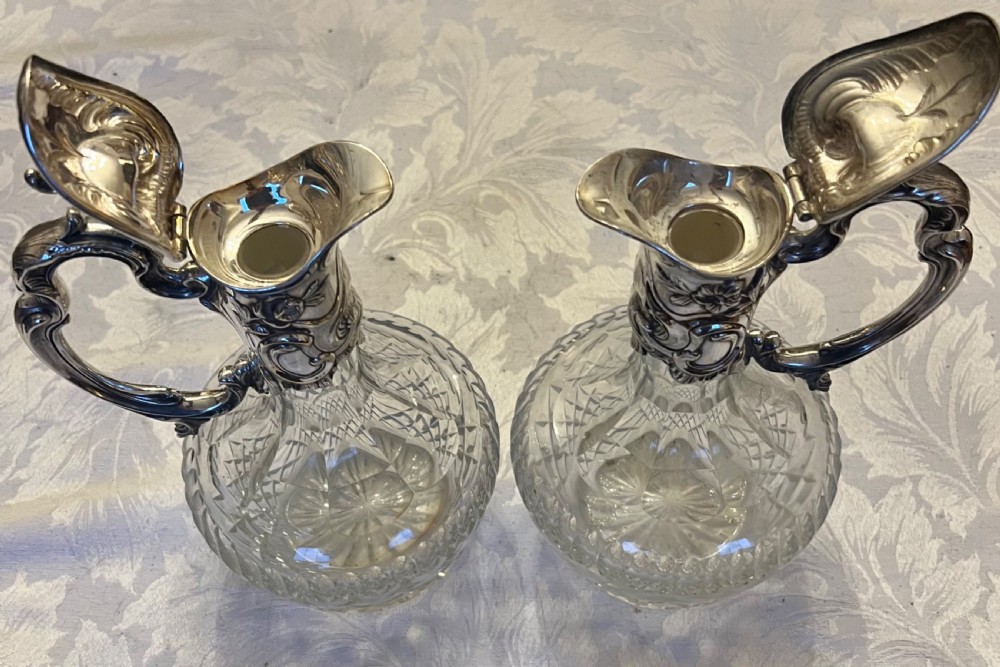 A pair of antique silver-plated claret jugs featuring ornate scroll handles, floral mounts, and diamond-pattern cut glass bodies. View II