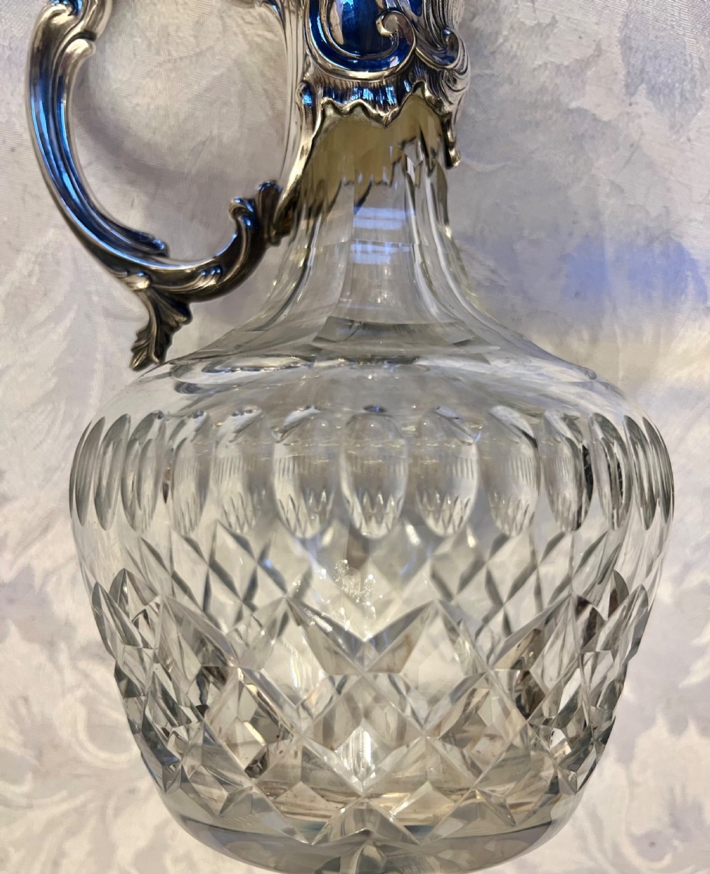 A pair of antique silver-plated claret jugs featuring ornate scroll handles, floral mounts, and diamond-pattern cut glass bodies. View IV