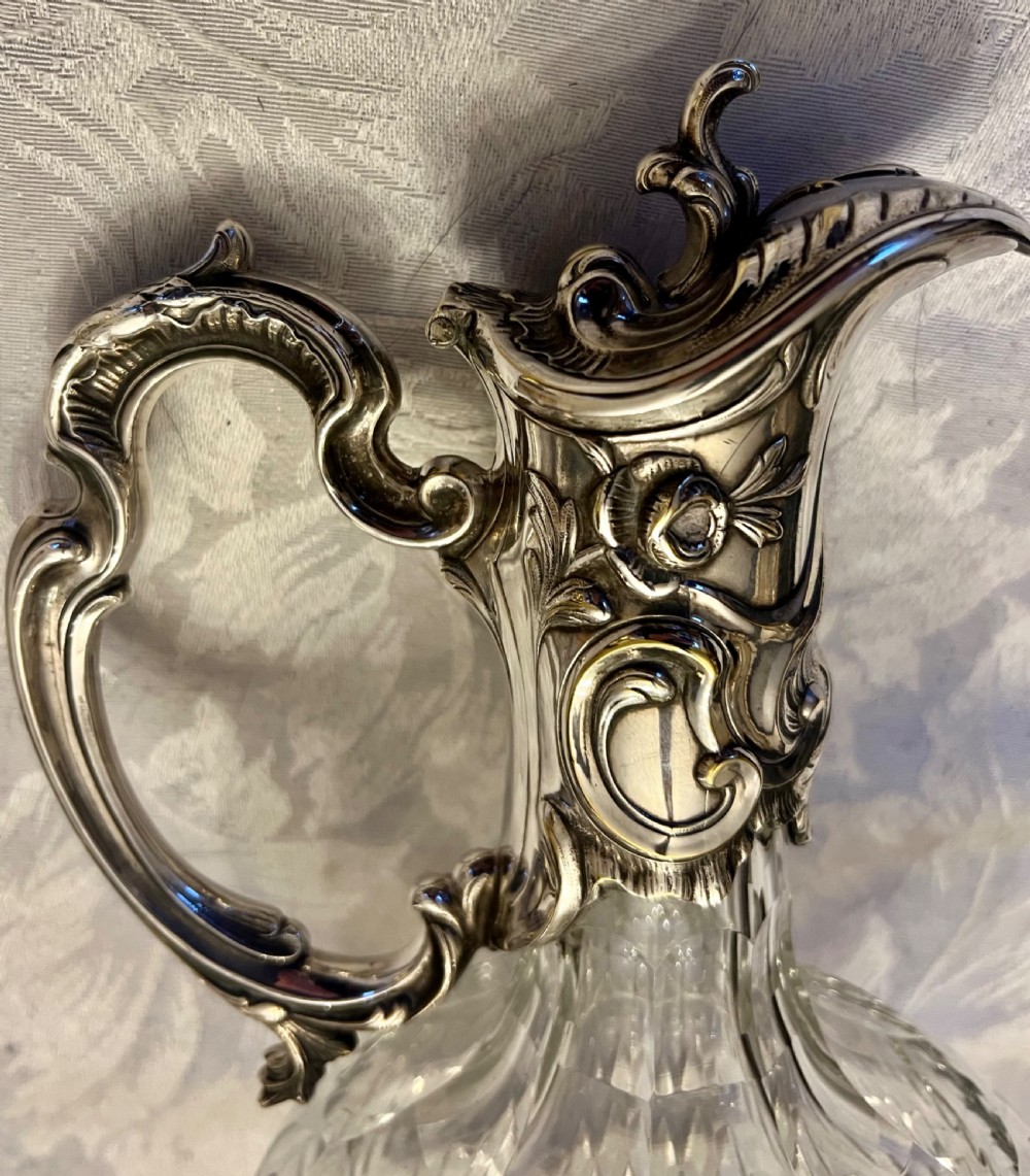 A pair of antique silver-plated claret jugs featuring ornate scroll handles, floral mounts, and diamond-pattern cut glass bodies. View V
