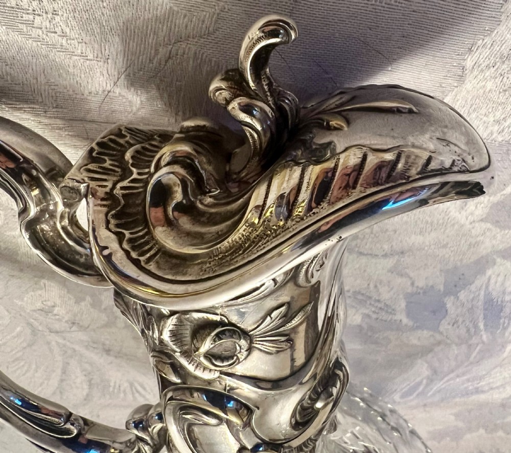 A pair of antique silver-plated claret jugs featuring ornate scroll handles, floral mounts, and diamond-pattern cut glass bodies. View VI