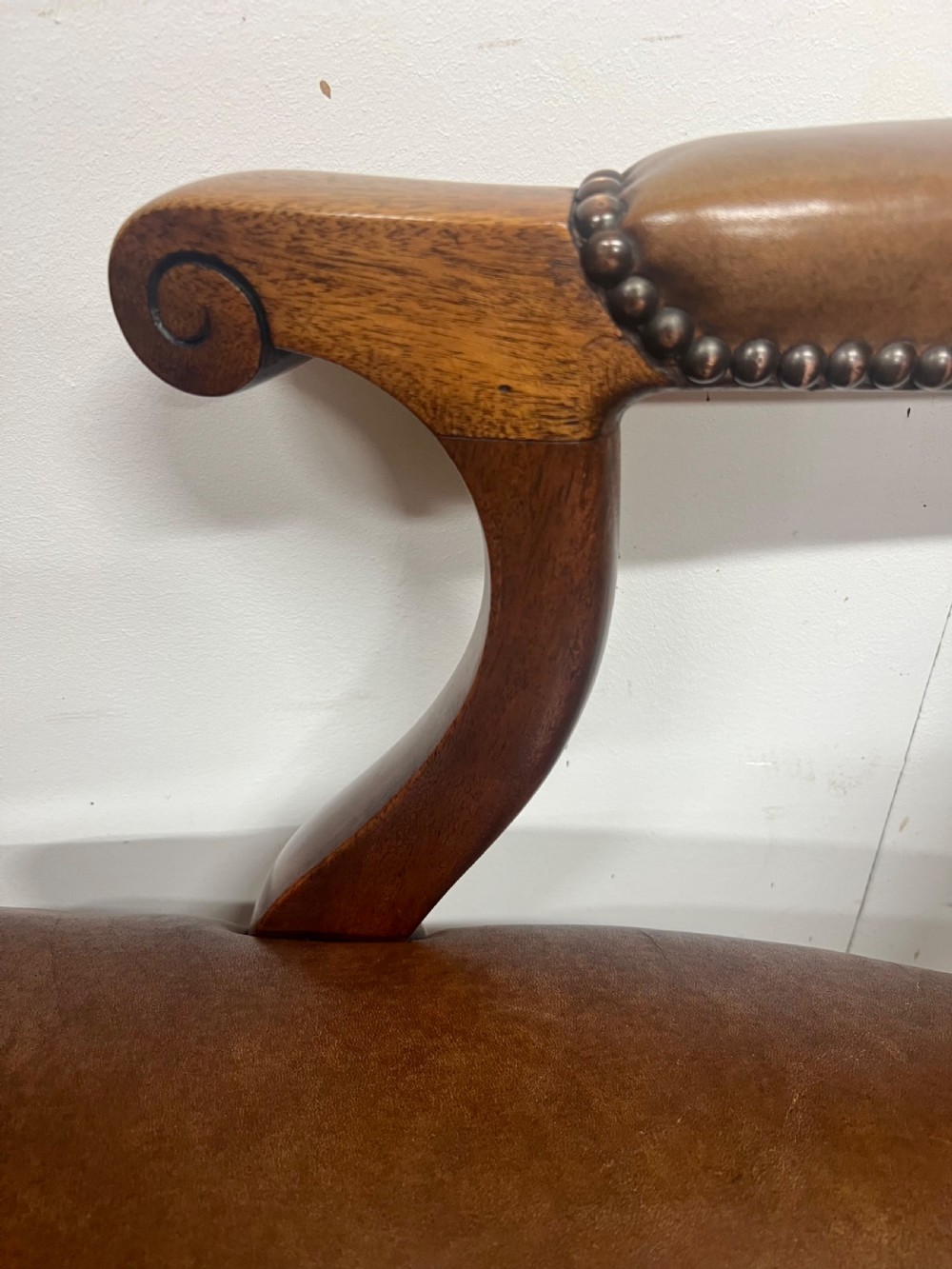 An antique brown leather upholstered elbow desk chair featuring a carved mahogany frame, cabriole front legs, padded seat and backrest, and brass stud trim. View IV
