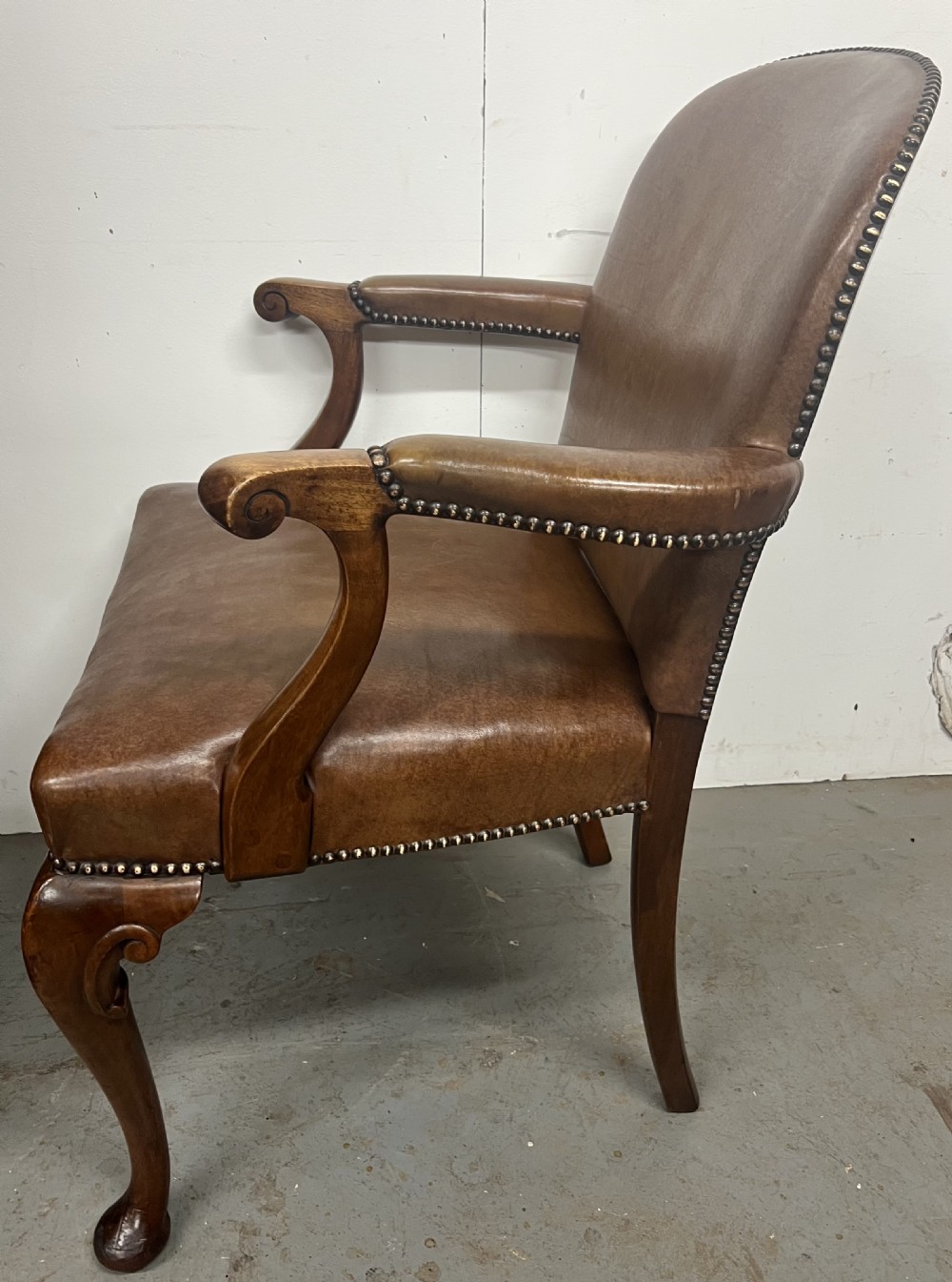 An antique brown leather upholstered elbow desk chair featuring a carved mahogany frame, cabriole front legs, padded seat and backrest, and brass stud trim. View VIII