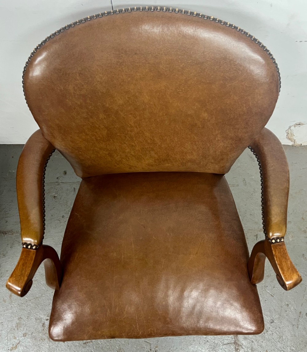 An antique brown leather upholstered elbow desk chair featuring a carved mahogany frame, cabriole front legs, padded seat and backrest, and brass stud trim. View IX