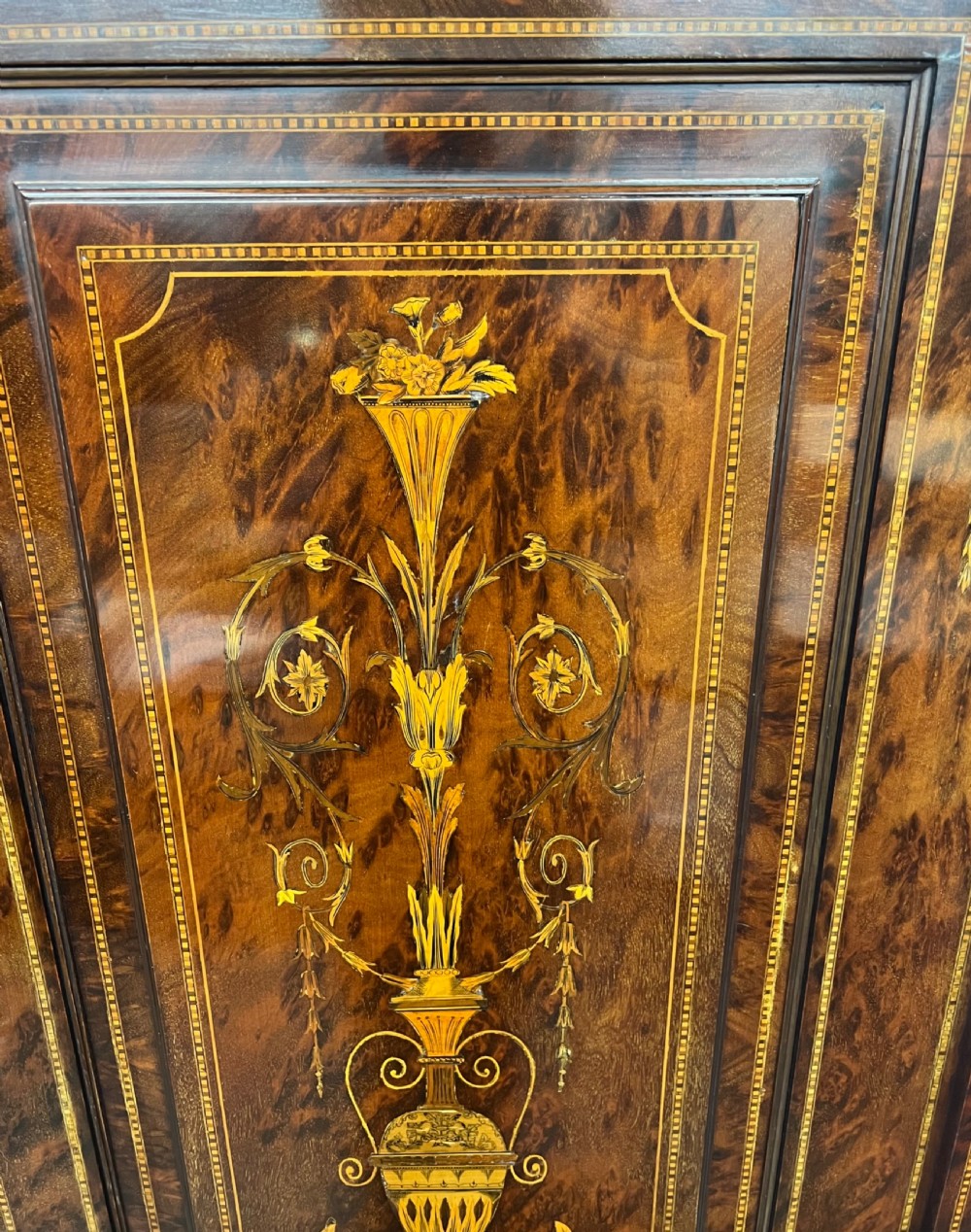 An antique dark mahogany linen press featuring classical marquetry urn inlay, a broken pediment top, two cabinet doors, and four lower drawers with circular brass handles. View III