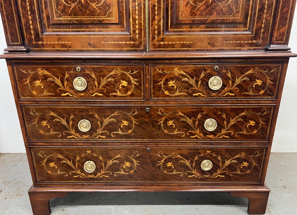 An antique dark mahogany linen press featuring classical marquetry urn inlay, a broken pediment top, two cabinet doors, and four lower drawers with circular brass handles. View IX