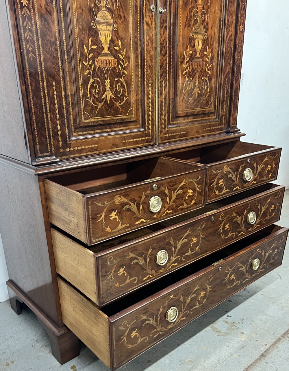 An antique dark mahogany linen press featuring classical marquetry urn inlay, a broken pediment top, two cabinet doors, and four lower drawers with circular brass handles. View XI