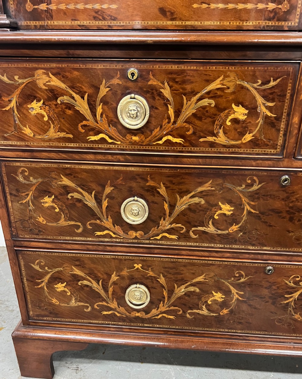 An antique dark mahogany linen press featuring classical marquetry urn inlay, a broken pediment top, two cabinet doors, and four lower drawers with circular brass handles. View XIV