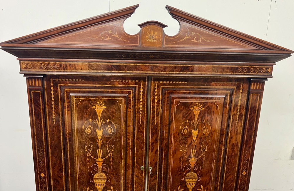 An antique dark mahogany linen press featuring classical marquetry urn inlay, a broken pediment top, two cabinet doors, and four lower drawers with circular brass handles. View XV