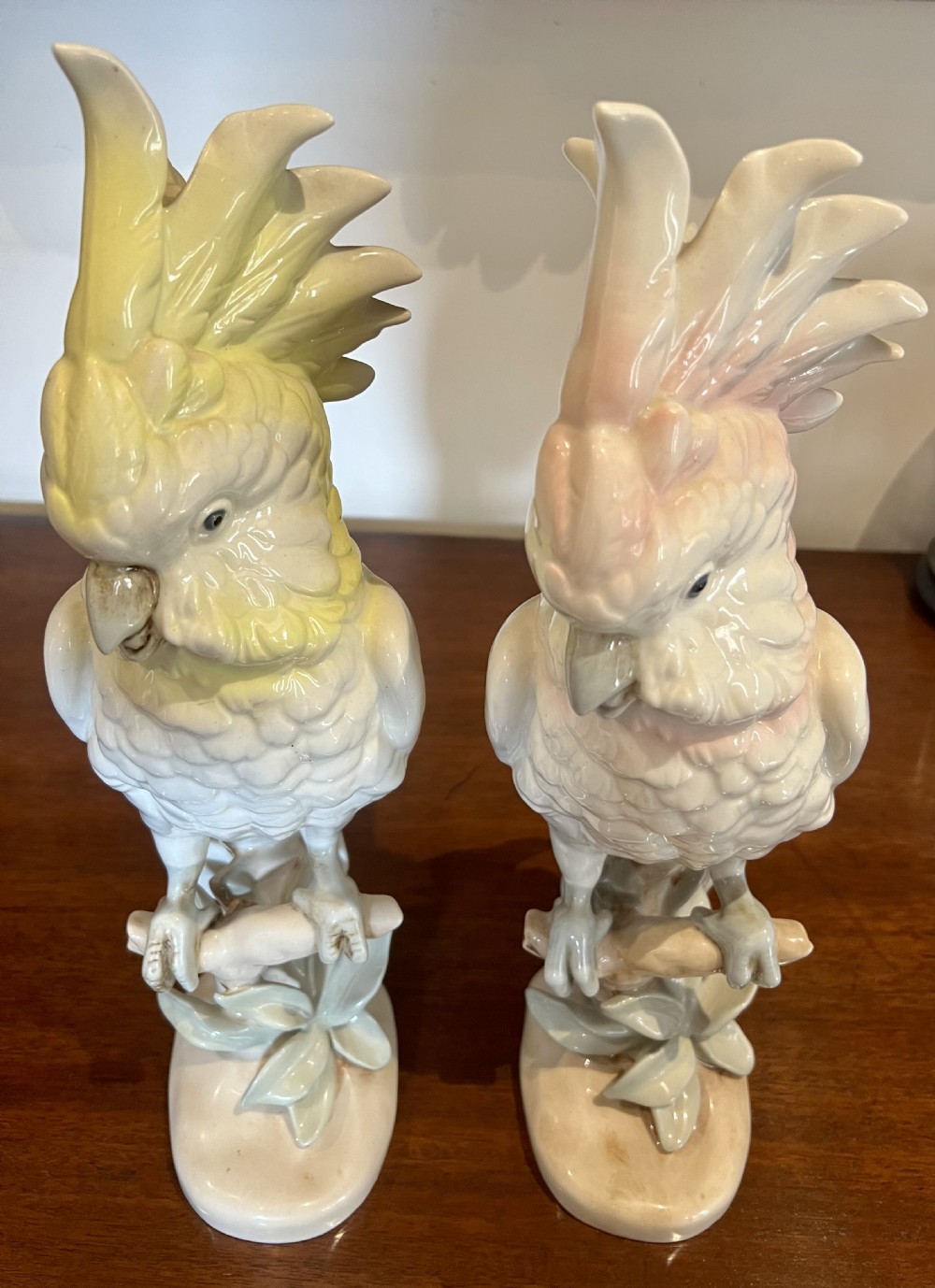 A pair of glazed porcelain cockatoo figurines perched on stylized foliage branches, one featuring a yellow crest and the other a soft pink crest. View II
