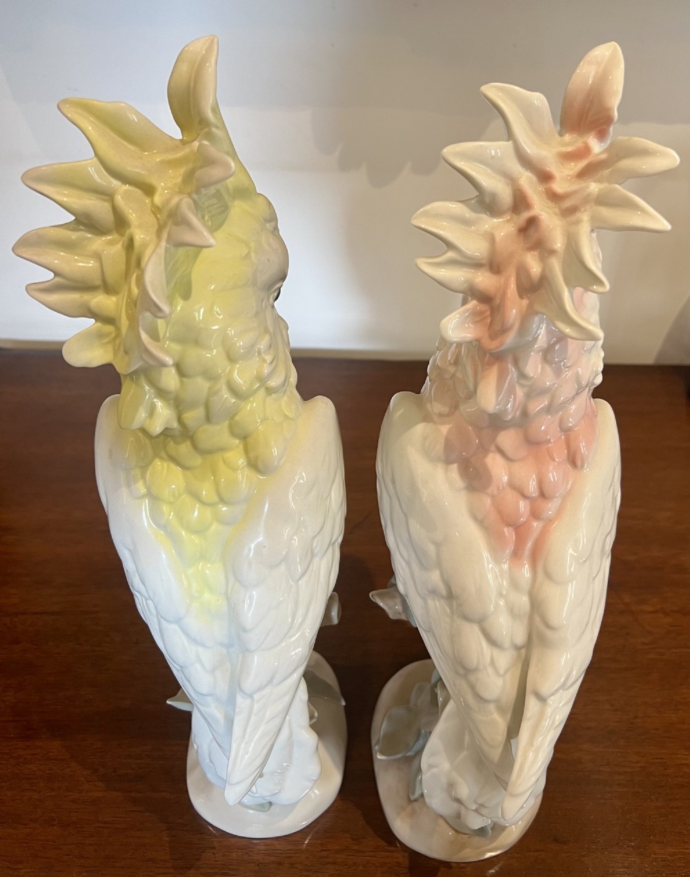 A pair of glazed porcelain cockatoo figurines perched on stylized foliage branches, one featuring a yellow crest and the other a soft pink crest. View III