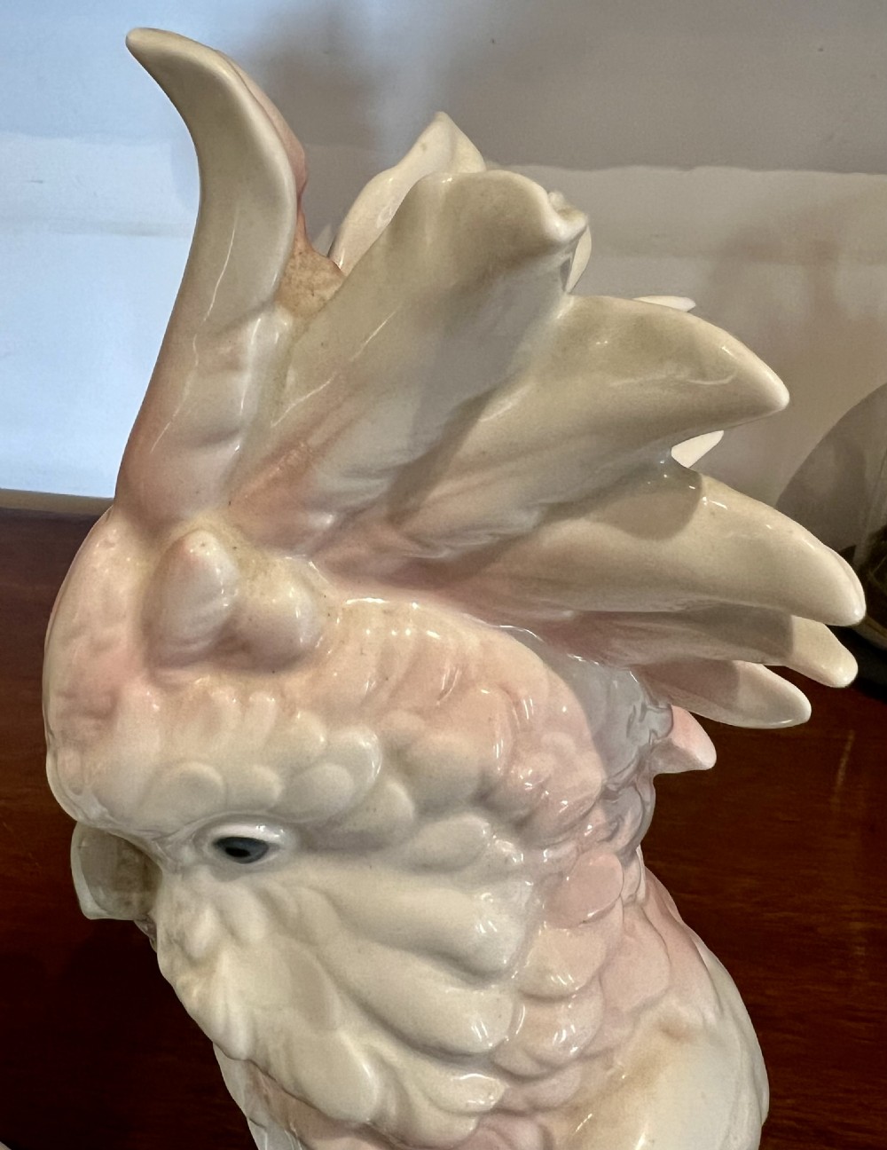 A pair of glazed porcelain cockatoo figurines perched on stylized foliage branches, one featuring a yellow crest and the other a soft pink crest. View V