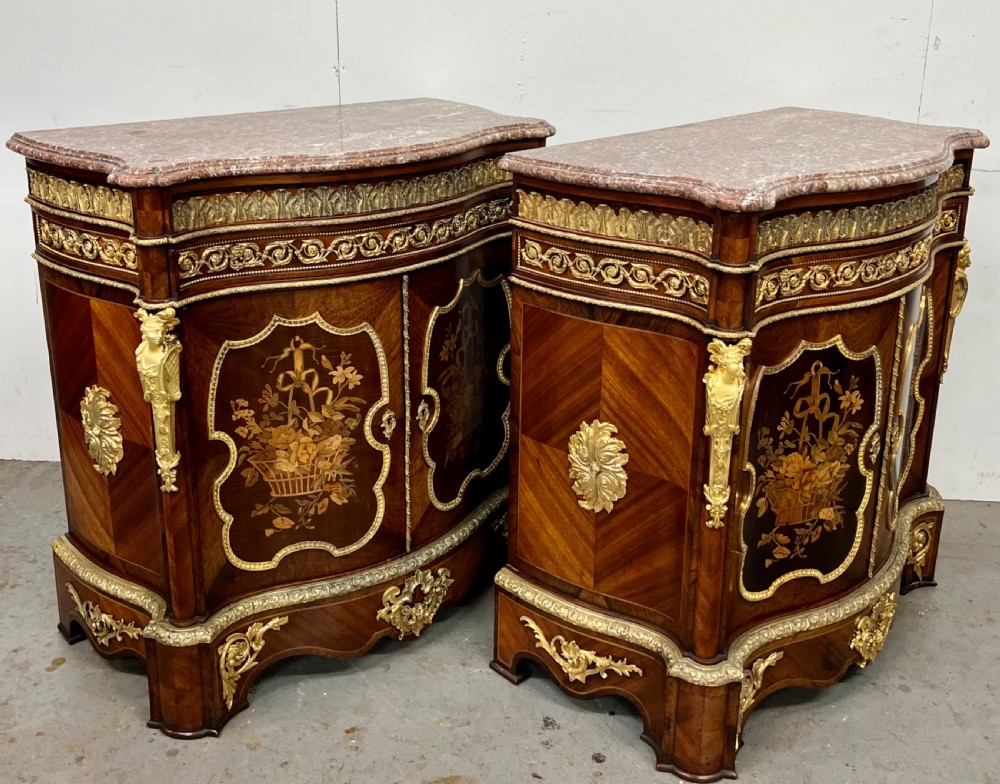 A pair of French Louis XV style kingwood side cabinets featuring floral marquetry, gilt-bronze ormolu mounts, and shaped pink marble tops.