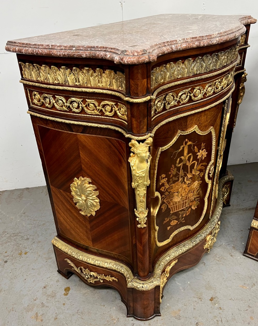 A pair of French Louis XV style kingwood side cabinets featuring floral marquetry, gilt-bronze ormolu mounts, and shaped pink marble tops. View XVI