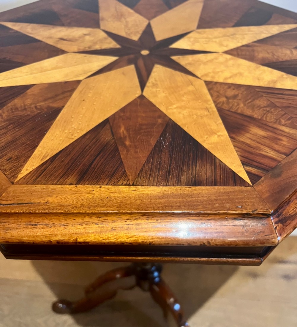 An octagonal antique specimen wood occasional table featuring a central geometric starburst marquetry top supported by a turned pedestal stem and tripod scroll feet. View II