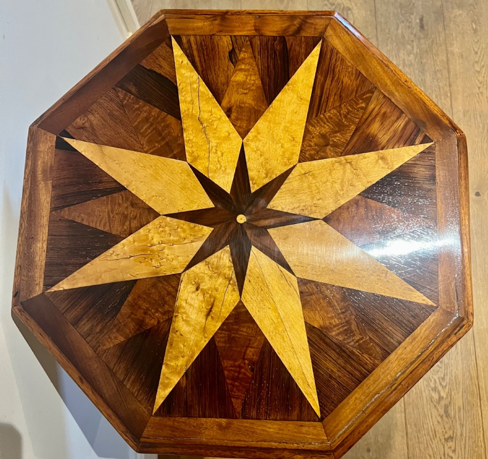 An octagonal antique specimen wood occasional table featuring a central geometric starburst marquetry top supported by a turned pedestal stem and tripod scroll feet. View III
