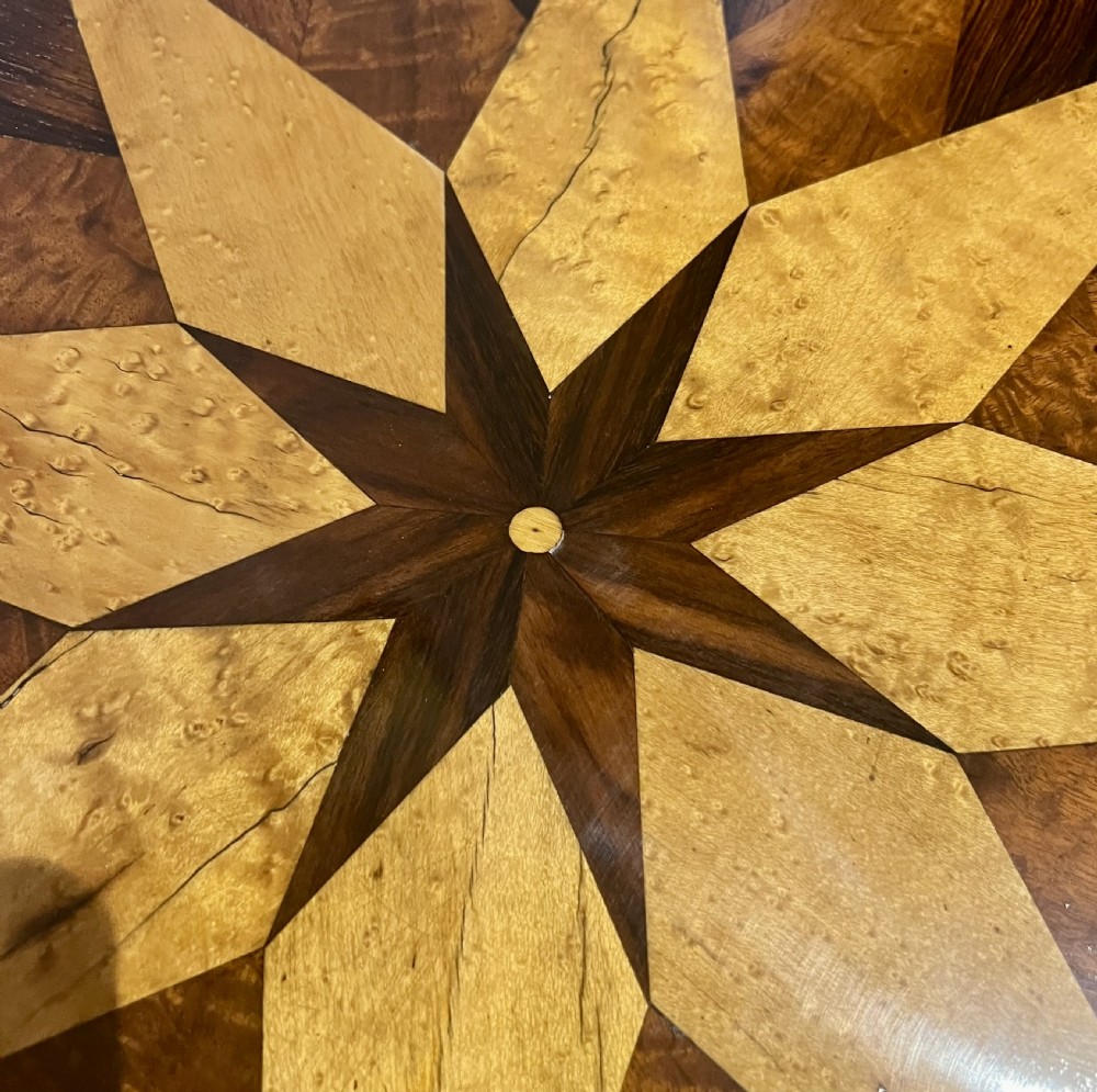 An octagonal antique specimen wood occasional table featuring a central geometric starburst marquetry top supported by a turned pedestal stem and tripod scroll feet. View V