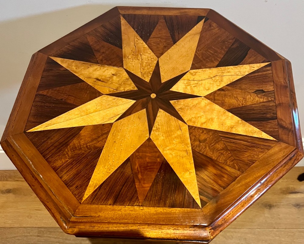 An octagonal antique specimen wood occasional table featuring a central geometric starburst marquetry top supported by a turned pedestal stem and tripod scroll feet. View VII