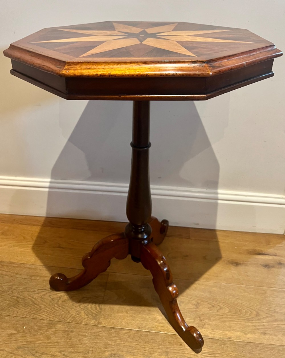 An octagonal antique specimen wood occasional table featuring a central geometric starburst marquetry top supported by a turned pedestal stem and tripod scroll feet. View IX