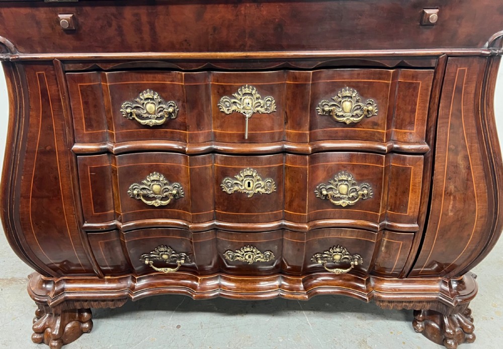 A Dutch burr walnut bureau with a slant-front writing slope, three contoured drawers, ornate brass handles, and carved claw and ball feet. View II