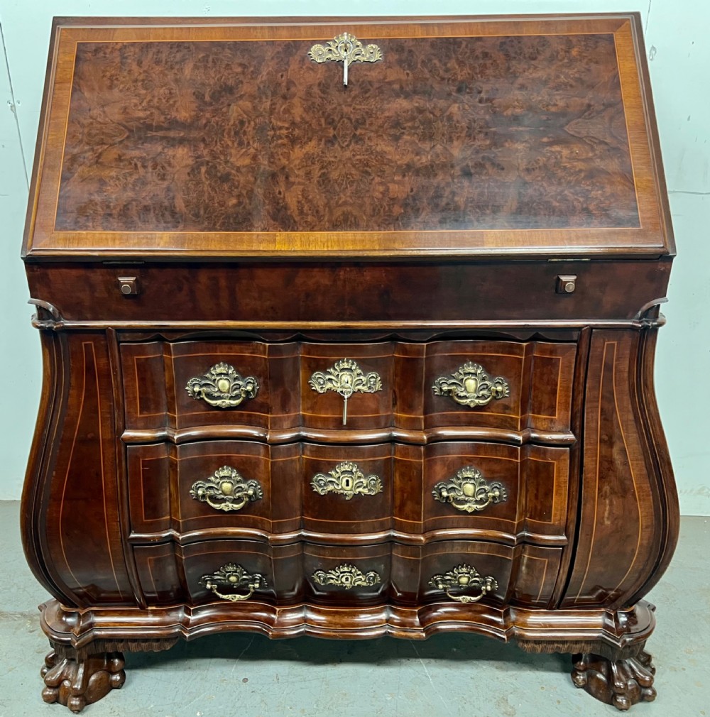 A Dutch burr walnut bureau with a slant-front writing slope, three contoured drawers, ornate brass handles, and carved claw and ball feet.