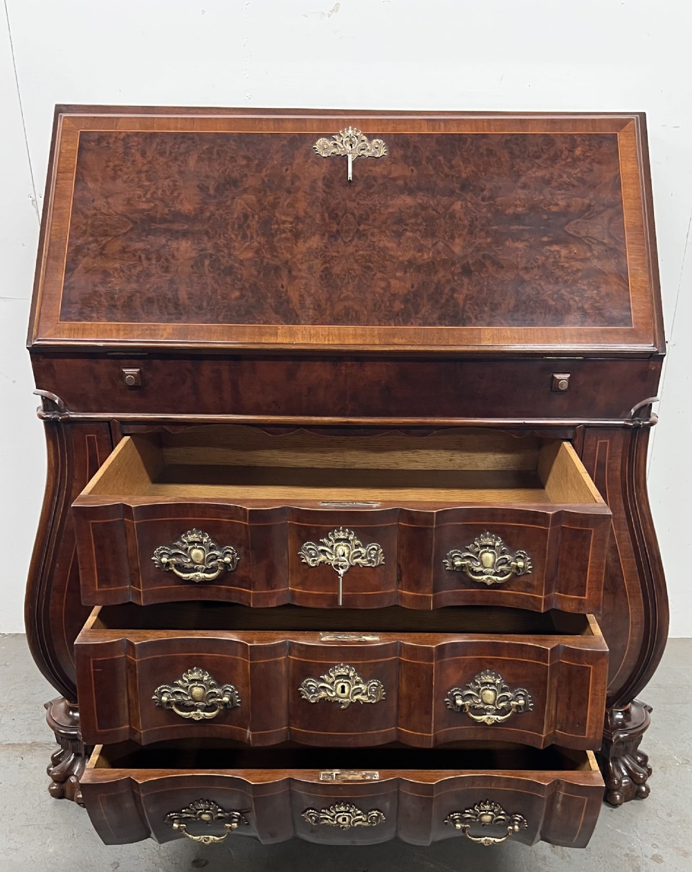 A Dutch burr walnut bureau with a slant-front writing slope, three contoured drawers, ornate brass handles, and carved claw and ball feet. View IX