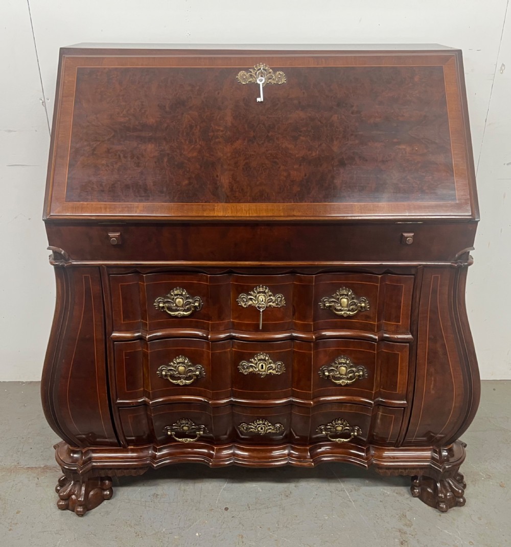 A Dutch burr walnut bureau with a slant-front writing slope, three contoured drawers, ornate brass handles, and carved claw and ball feet. View X