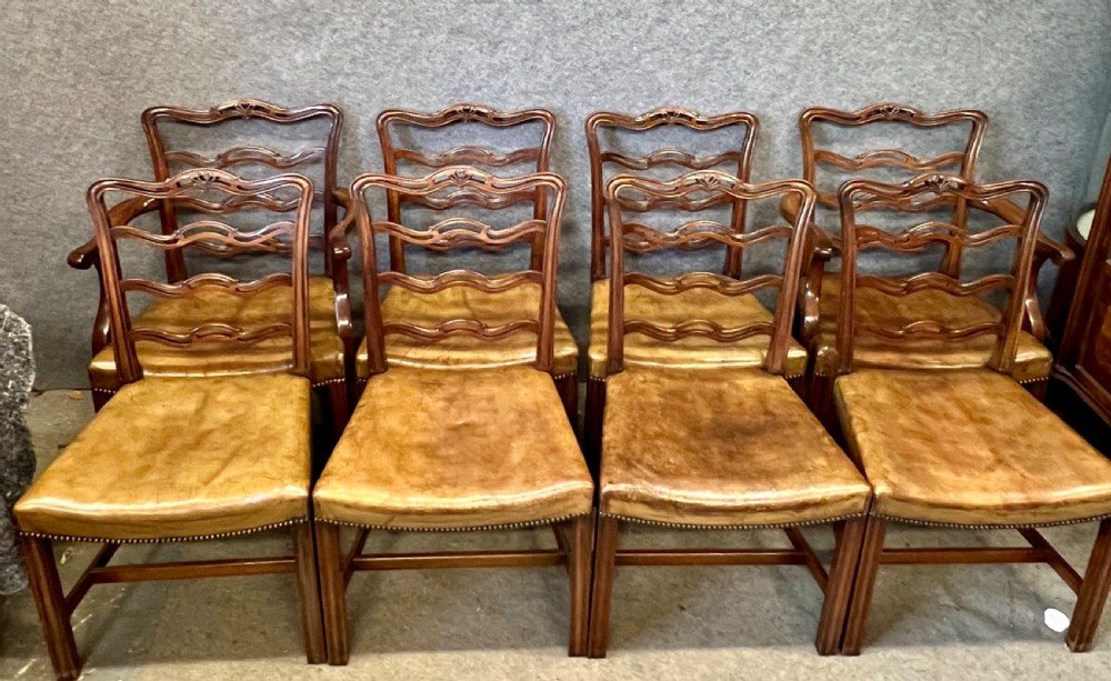 A set of eight Chippendale style mahogany dining chairs featuring serpentine ladderback splats and tan leather drop-in seats, including six side chairs and two carver armchairs.