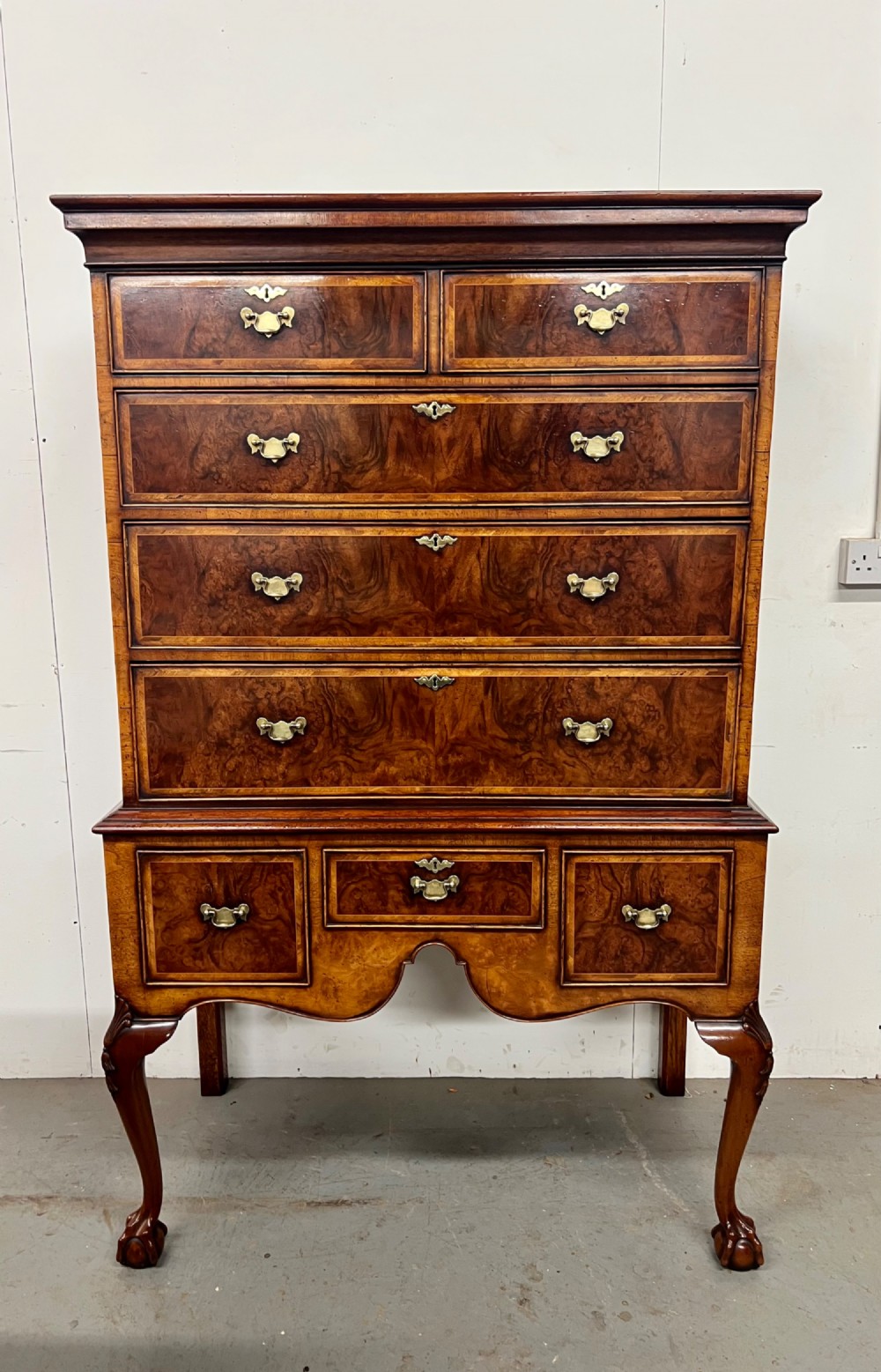 A tall burr walnut chest on stand featuring two short over three long drawers on top, three lower drawers, a shaped apron, and carved cabriole legs.