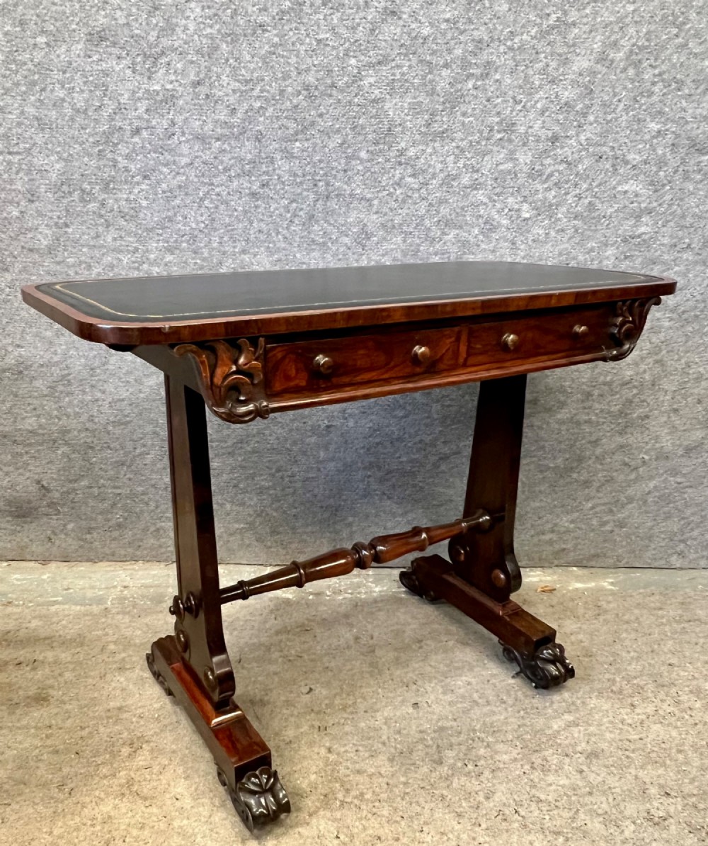A Regency period dark rosewood freestanding writing table featuring a dark leather insert top, carved scroll accents, a turned central stretcher, and carved feet.