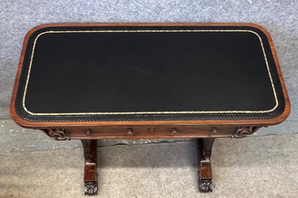 A Regency period dark rosewood freestanding writing table featuring a dark leather insert top, carved scroll accents, a turned central stretcher, and carved feet. View III