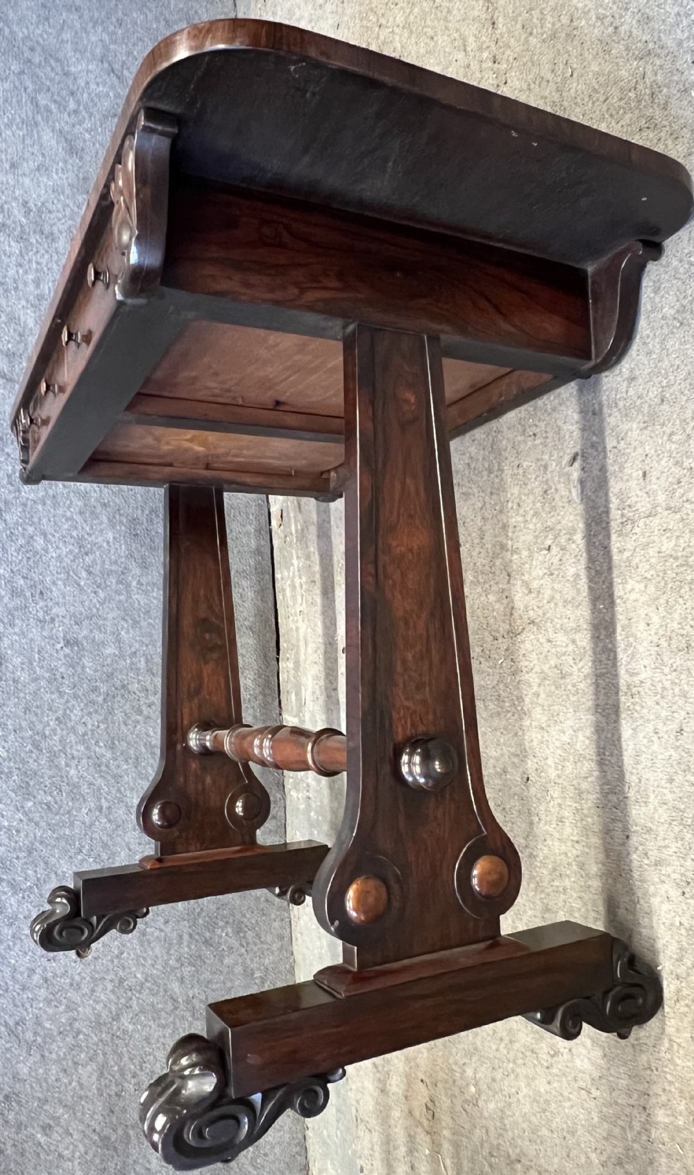 A Regency period dark rosewood freestanding writing table featuring a dark leather insert top, carved scroll accents, a turned central stretcher, and carved feet. View VII