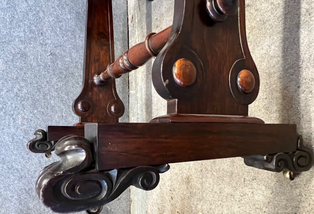A Regency period dark rosewood freestanding writing table featuring a dark leather insert top, carved scroll accents, a turned central stretcher, and carved feet. View VIII