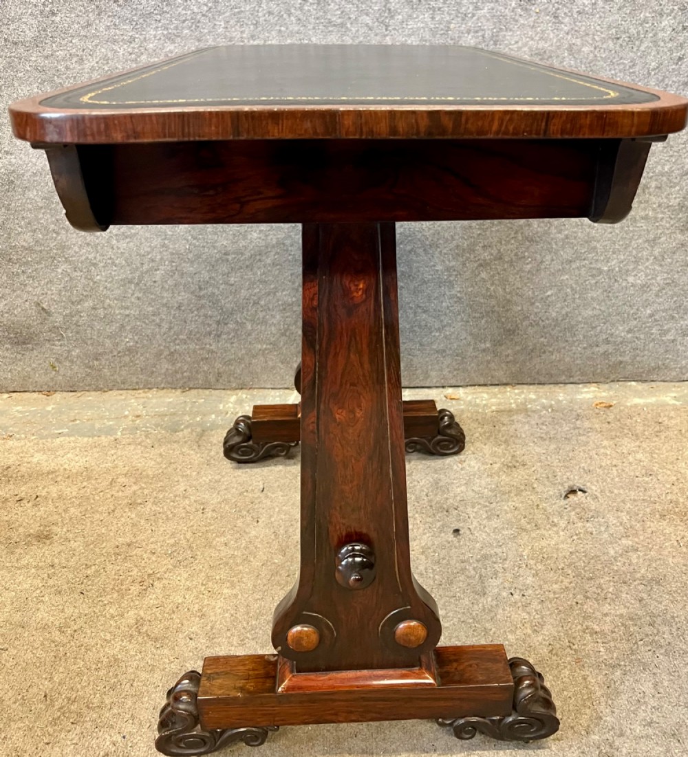 A Regency period dark rosewood freestanding writing table featuring a dark leather insert top, carved scroll accents, a turned central stretcher, and carved feet. View IX