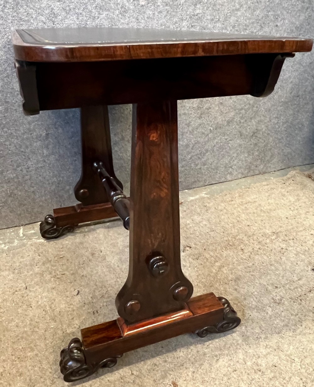 A Regency period dark rosewood freestanding writing table featuring a dark leather insert top, carved scroll accents, a turned central stretcher, and carved feet. View XI