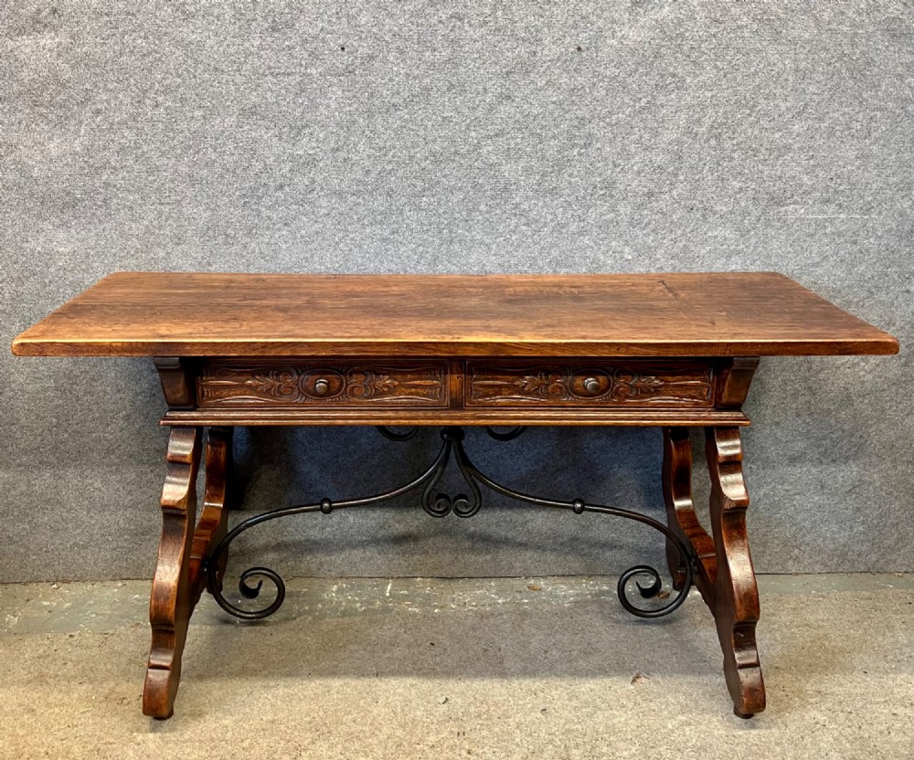 A dark oak Spanish console table featuring two carved drawers, lyre-shaped trestle legs, and a scrolled wrought iron stretcher.