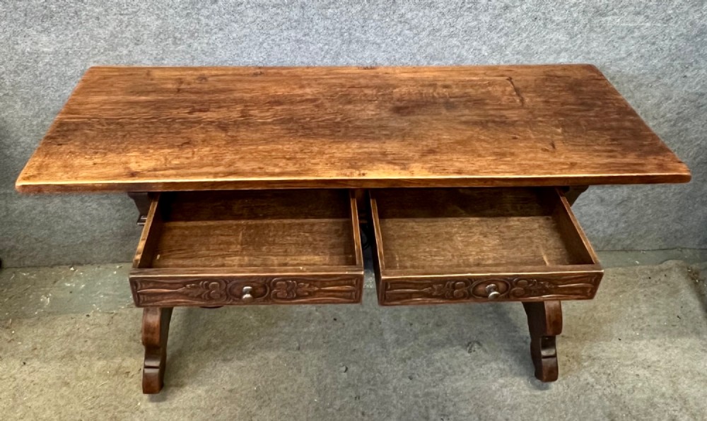 A dark oak Spanish console table featuring two carved drawers, lyre-shaped trestle legs, and a scrolled wrought iron stretcher. View II