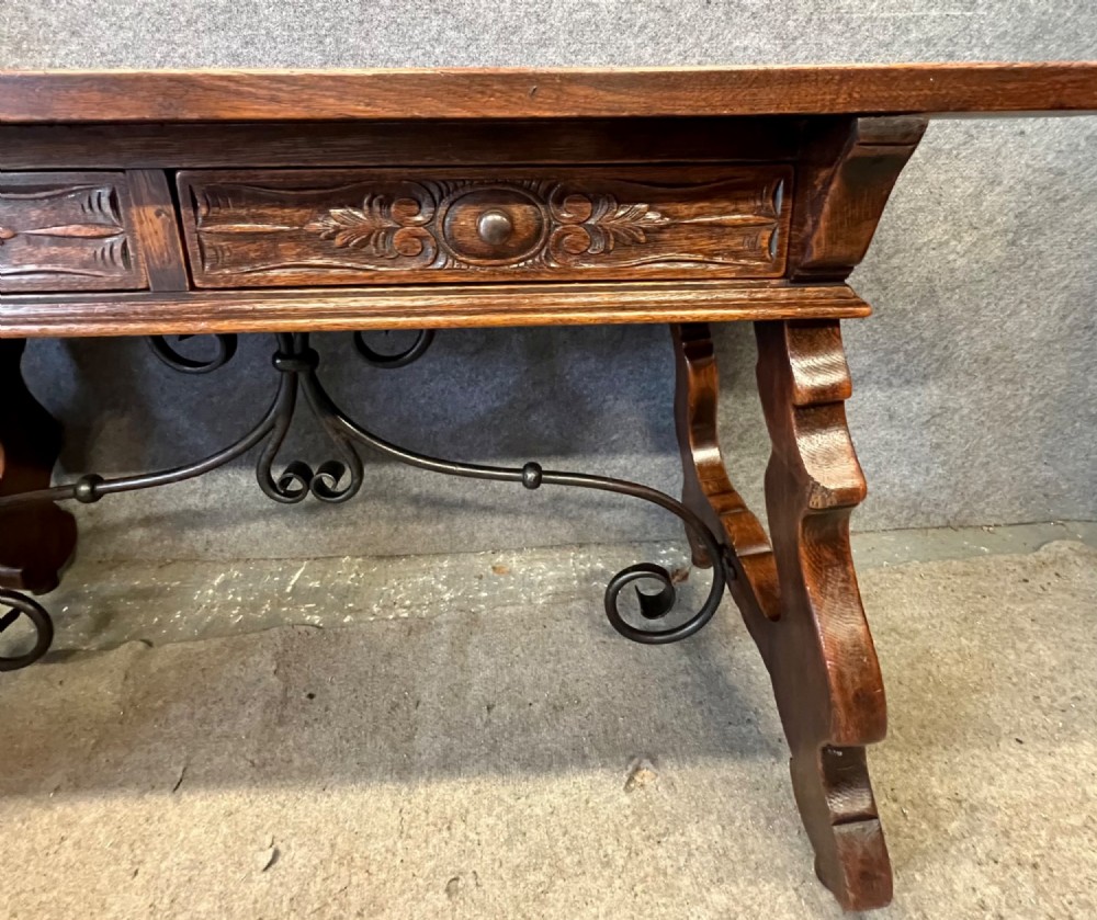 A dark oak Spanish console table featuring two carved drawers, lyre-shaped trestle legs, and a scrolled wrought iron stretcher. View III