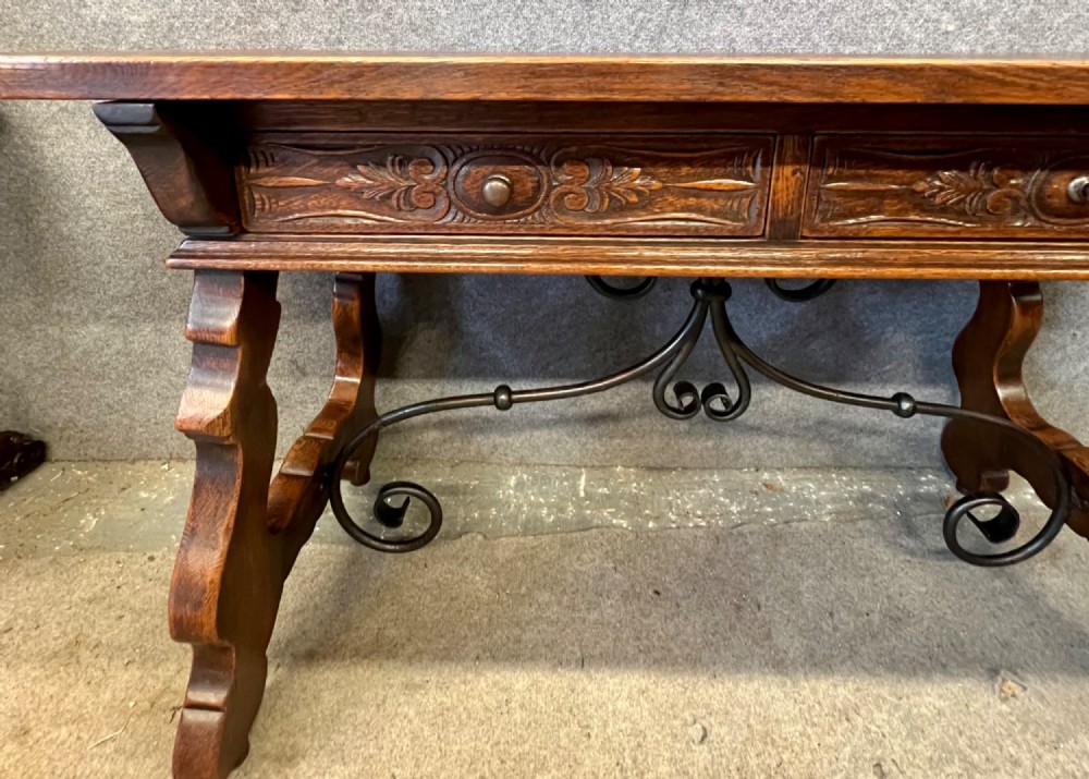 A dark oak Spanish console table featuring two carved drawers, lyre-shaped trestle legs, and a scrolled wrought iron stretcher. View IV