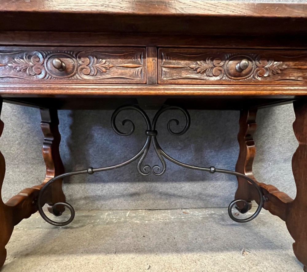 A dark oak Spanish console table featuring two carved drawers, lyre-shaped trestle legs, and a scrolled wrought iron stretcher. View V