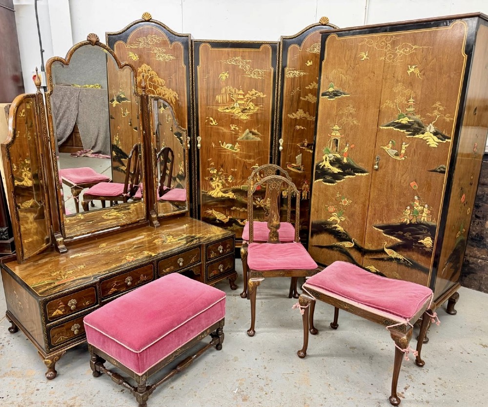A multi-piece lacquered timber Chinoiserie bedroom suite by Maples and Co, featuring a dressing table with a triple mirror, wardrobes with gilt landscape scenes, and pink velvet upholstered stools.