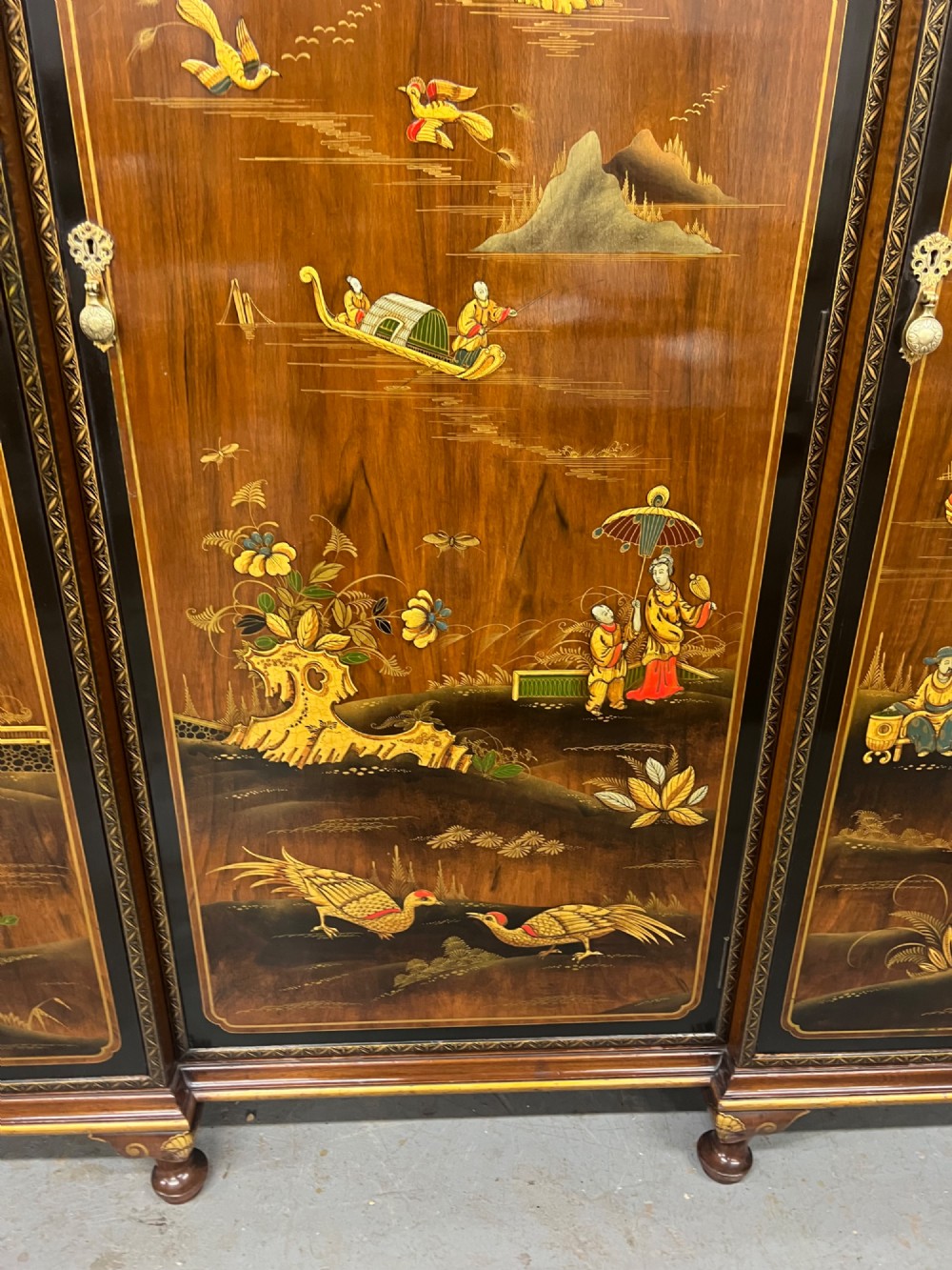 A multi-piece lacquered timber Chinoiserie bedroom suite by Maples and Co, featuring a dressing table with a triple mirror, wardrobes with gilt landscape scenes, and pink velvet upholstered stools. View IX