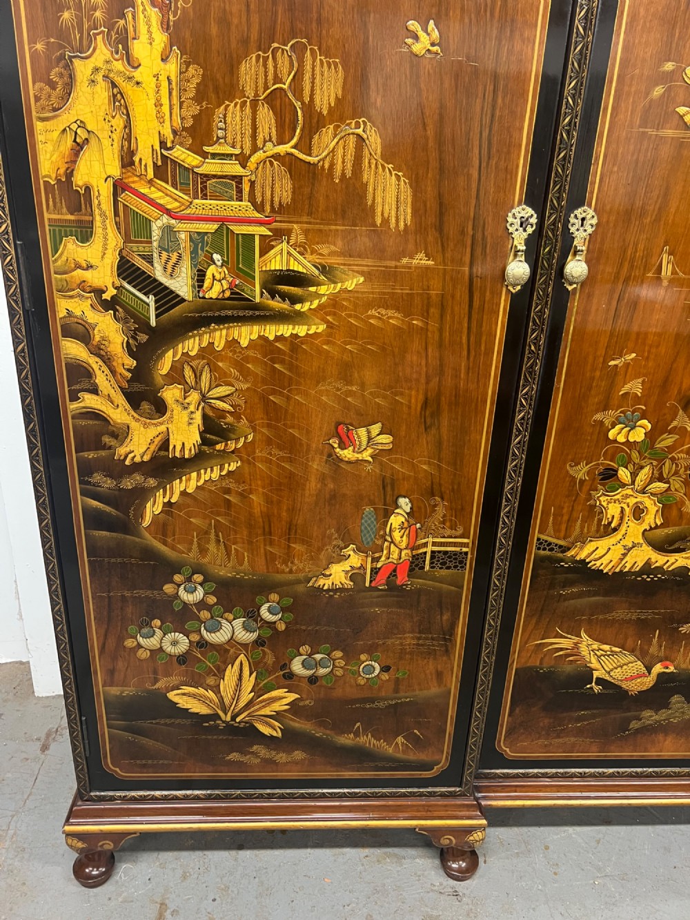 A multi-piece lacquered timber Chinoiserie bedroom suite by Maples and Co, featuring a dressing table with a triple mirror, wardrobes with gilt landscape scenes, and pink velvet upholstered stools. View X